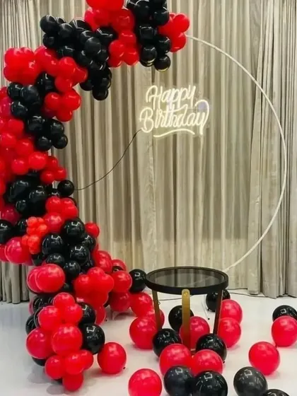 A striking and modern birthday decoration using a simple color palette. I created a half-arch of red and black balloons on a white circular frame, with a neon sign and a small table for the cake.