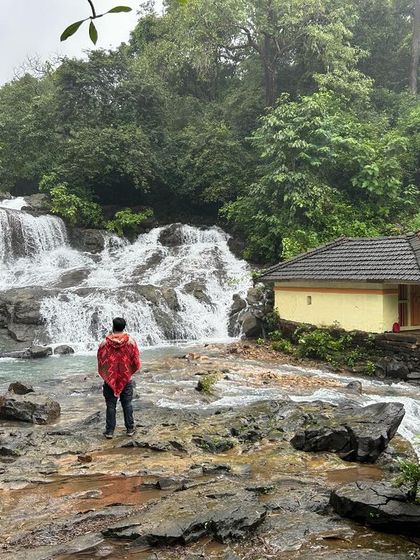 A lone trekker admiring the view of a waterfall and temple at Melinaguli, capturing the essence of monsoon beauty in Uttara Kannada.