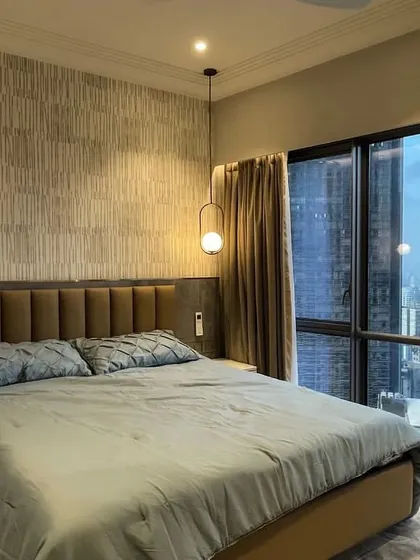 This bedroom at Lodha World One balances a stunning city view with a calm, Art Deco-inspired interior. The textured wallpaper and elegant pendant lights create a sophisticated retreat high above Mumbai.
