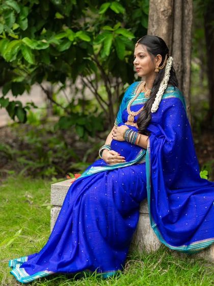The royal blue saree drapes beautifully in this serene outdoor setting, creating a picture of calm and elegance as she awaits her little one.