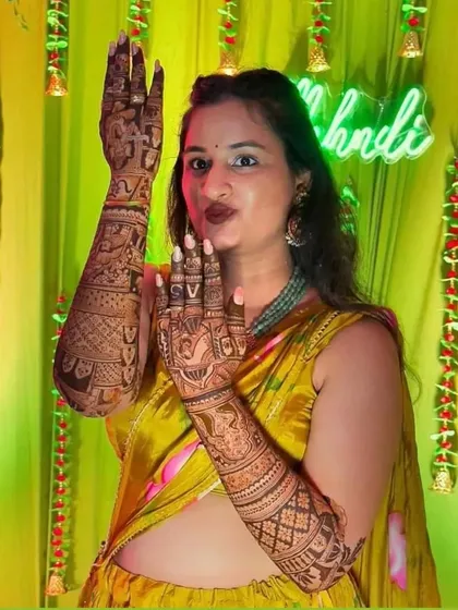 A happy bride posing and showing off her full arm mehendi at her ceremony.