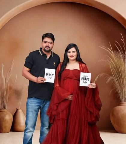 A stylish studio portrait where the couple holds "Daddy to be" and "Mom to be" signs. The earthy tones of the backdrop create a modern and warm feel for their announcement.