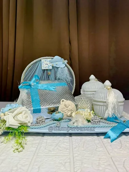 A luxurious baby boy announcement hamper on a tray, featuring silver and blue elements, decorative jars, and flowers.