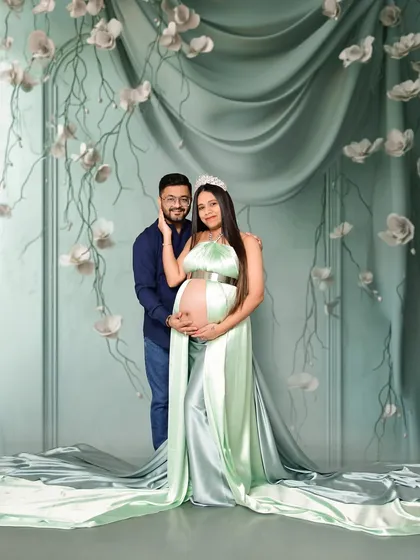 A glamorous maternity portrait featuring a satin gown with a long train against an elegant, textured backdrop. The use of a tiara and soft lighting gives this image a fairytale-like quality, perfect for a queen awaiting her heir.
