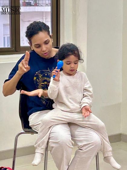A mother guides her child in playing a percussion instrument. Our classes empower parents to become active participants in their child's musical education.
