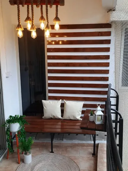 This urban balcony design is all about a clean, classy, and comfortable look. We used polished pinewood for the wall paneling and bench, and added a custom rope and bamboo hanging lamp to create a warm, inviting glow for the evenings.