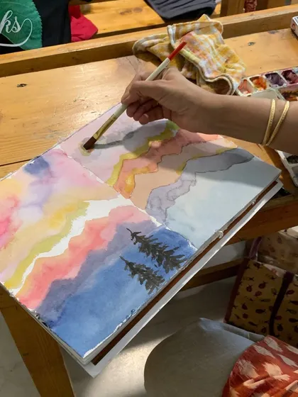 A student experiments with abstract watercolor landscapes, playing with color washes and simple tree forms. We encourage creative exploration alongside technical skill-building.