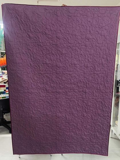 The back of a memory quilt made from a daughter's t-shirts and frocks, showing a solid purple fabric that highlights the quilting.