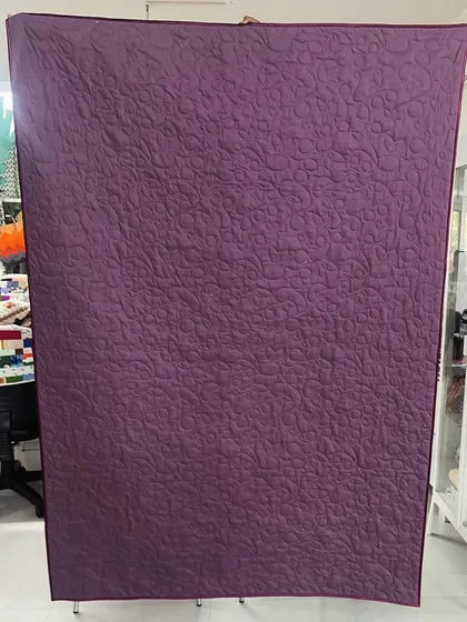 The back of a memory quilt made from a daughter's t-shirts and frocks, showing a solid purple fabric that highlights the quilting.