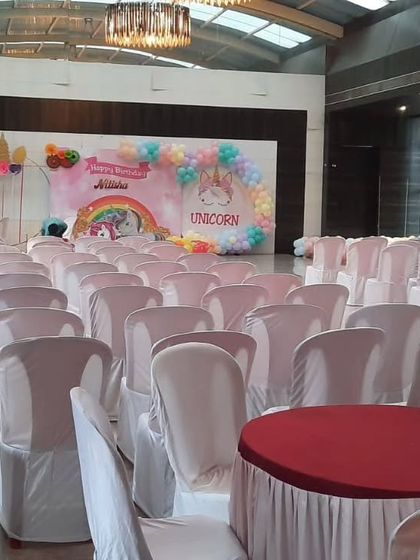 A unicorn-themed birthday party in a large hall. The pastel-colored backdrop and balloon decorations create a magical atmosphere for the celebration.