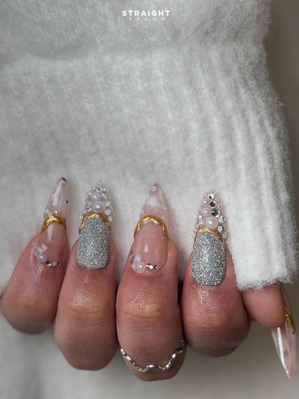 The ultimate glam set. These long, clear stiletto nails are loaded with silver glitter, caviar beads, pearls, and gold accents for a truly extravagant look.