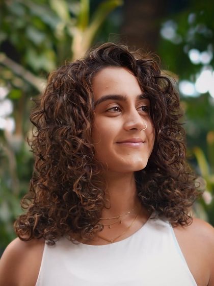 A profile shot capturing the soft, natural look of these highlighted curls in a beautiful outdoor setting.