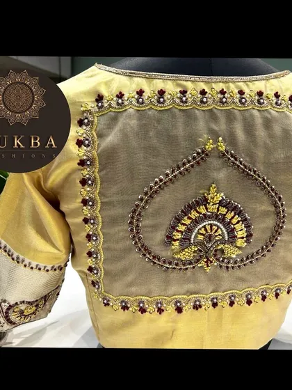 A sophisticated gold blouse with a sheer back panel. The centerpiece is a beautifully embroidered heart-shaped motif, framed with delicate beadwork for a simple yet elegant look.