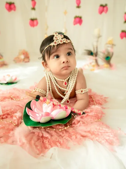 A thoughtful moment from a little Krishna. The delicate props like the lotus flower add a beautiful and symbolic touch to the Janmashtami theme.