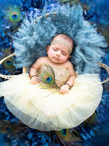 A sleeping baby Radha, looking peaceful and angelic in a basket of blue flowers.