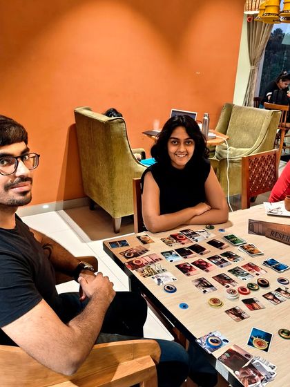 A couple enjoys a two-player game of 'Splendor'. My cafe is a great place for a casual date night filled with friendly competition.