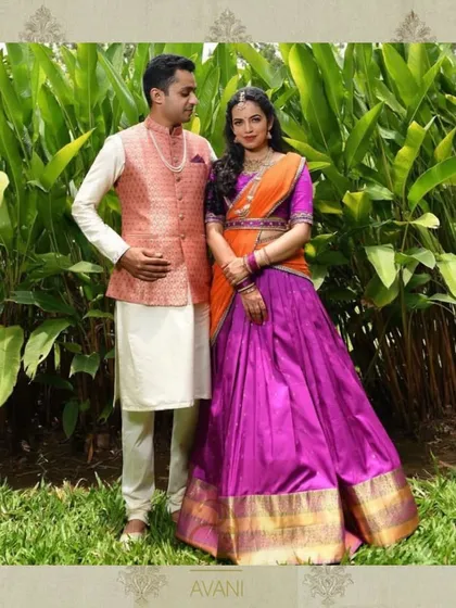 A couple posing in their traditional attire. The client wears a vibrant purple and orange half-saree, a beautiful and colorful choice for an engagement or other ceremony.