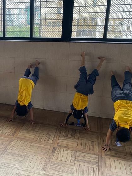 Young students practice wall-assisted handstands. This is a great exercise for building upper body strength, balance, and confidence in our introductory gymnastics program.
