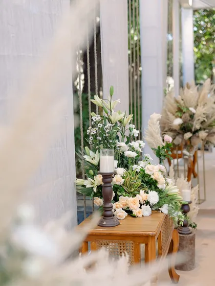 A close-up of a floral arrangement on a wooden console table, part of a chic and airy boho-themed Roka ceremony.