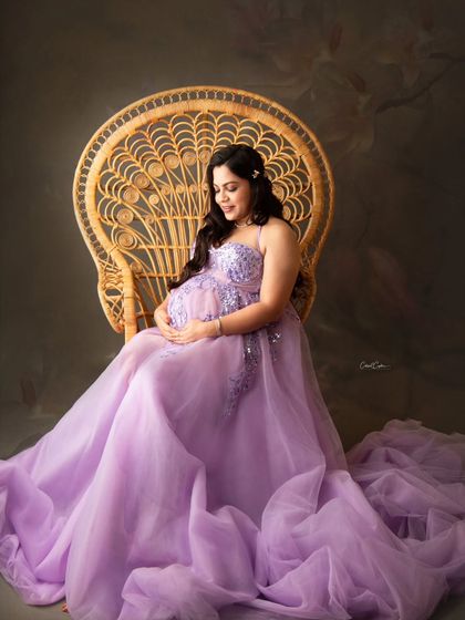 A quiet, contemplative moment on the peacock throne. The mom-to-be looks down at her bump, surrounded by the flowing lavender fabric of her gown.
