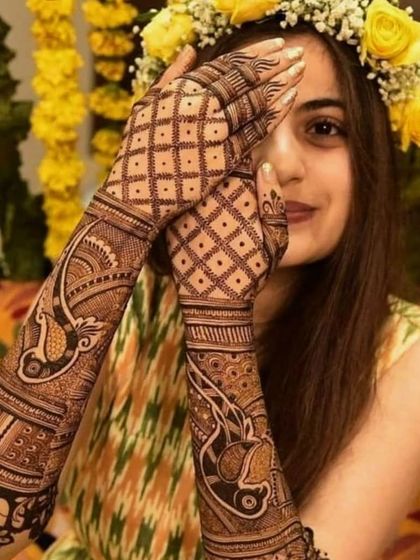 A beautiful bride peeks through her hands, which are adorned with a lovely peacock and check-patterned design.