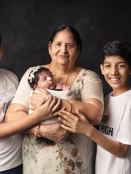 A grandmother's love is so special. Here, she holds her new grandchild while two proud older brothers stand by her side, creating a heartwarming memory.