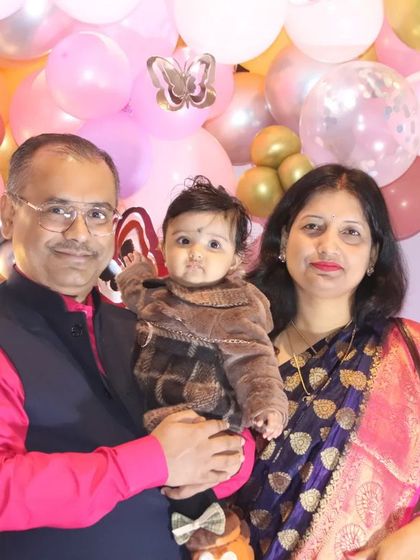 A family portrait taken against a backdrop of pink and gold balloons. This photo captures the family celebrating their little one's special day.