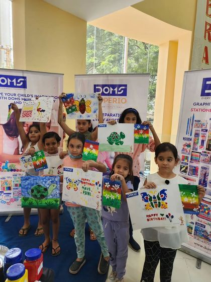 A group of girls proudly hold up their colorful paintings and birthday cards. Each piece is unique and full of personality.