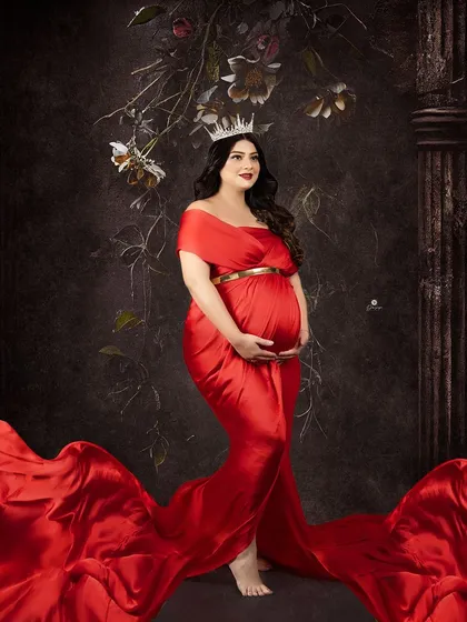A regal portrait of a mom-to-be in a flowing red satin gown, complete with a crown. This look is perfect for clients who want to feel like royalty during their maternity shoot.