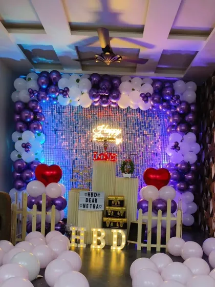 This birthday decoration uses a beautiful purple and white color palette. The floor is covered in light-colored balloons, making the space feel bright and airy.