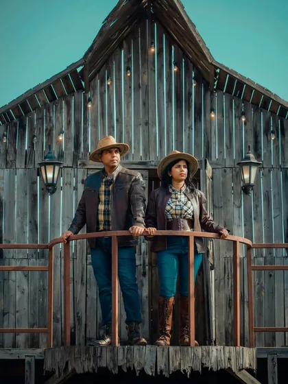 A dramatic shot from a rustic, barn-themed pre-wedding shoot. Aditya and Priyanka look out from a balcony, creating a cinematic and powerful image.