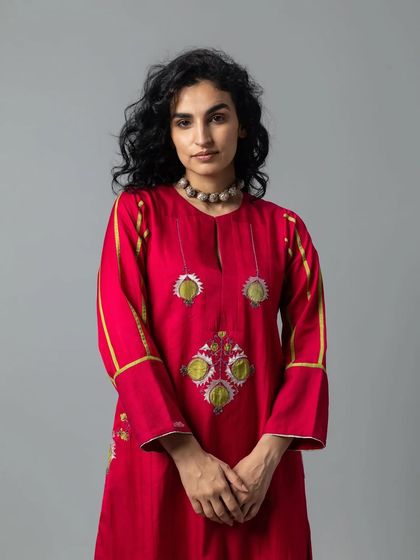 A model in a vibrant red kurta set with unique, appliqué-style embroidery on the front and sleeves, creating a modern yet traditional look.