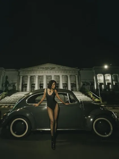 A wide shot from the same series, placing the car and model against the iconic backdrop of The Asiatic Society of Mumbai library. This is automotive fashion at its most atmospheric.