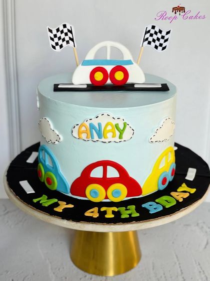 A cute and colorful car-themed cake for a 4th birthday. The cake board is designed to look like a road, and the cake itself is decorated with fun, cartoonish cars.
