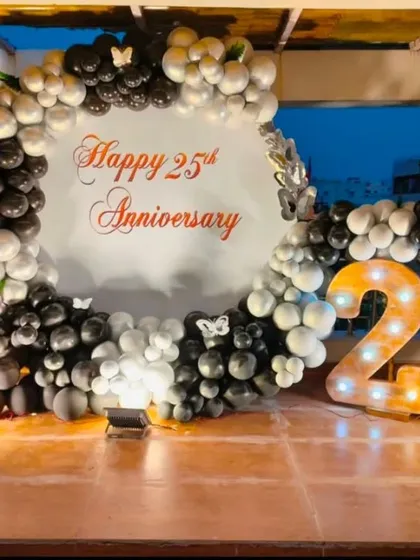 An elegant 25th-anniversary party on a rooftop. This setup features a circular backdrop with custom text, a black and silver balloon garland, and large marquee numbers.