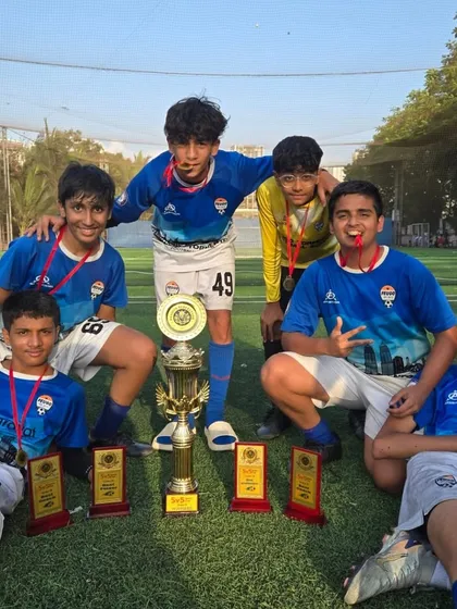 The U-15 champions relaxing on the pitch with their medals and trophies after a hard-fought tournament.