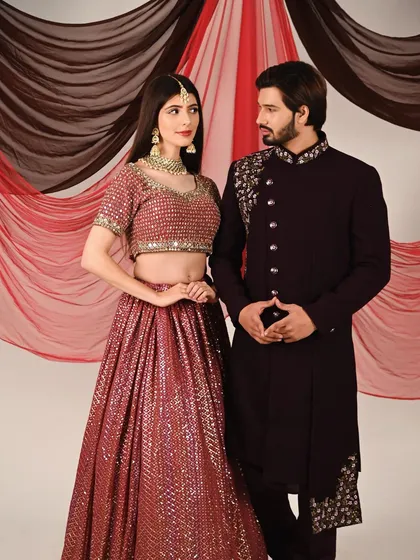 An ethnic wear photoshoot featuring a couple in coordinated outfits. Her sequined lehenga and his embroidered sherwani are a perfect match.