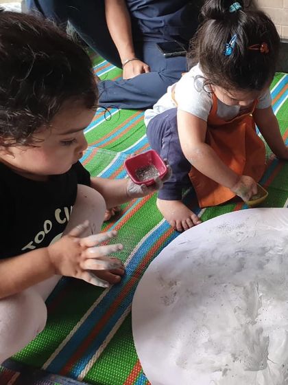 Exploring the texture of the moon's surface. Here, two children are using their hands to play with a flour and glitter mixture on a large paper moon.