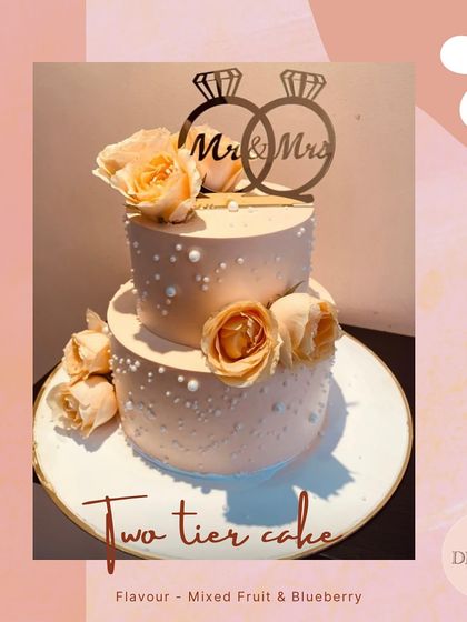 A classic two-tier anniversary cake with a 'Mr & Mrs' topper. Adorned with soft-hued roses and delicate pearls, this cake combines Mixed Fruit and Blueberry flavors for a delightful taste.
