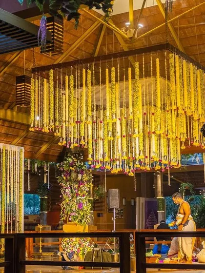 The wedding mandap setup, featuring a magnificent floral chandelier and a backdrop of hanging flower strings, ready for the ceremony.
