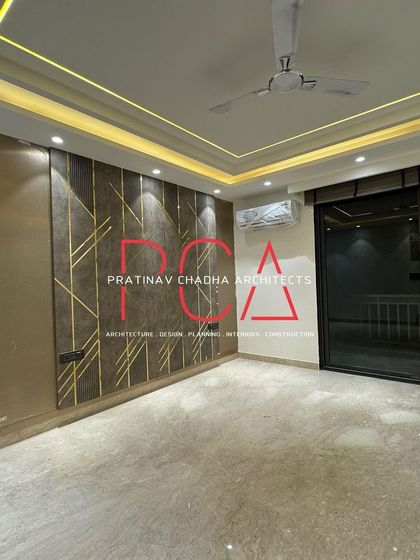 An elegant living space in our Vasant Kunj project, featuring a feature wall with metallic gold inlay work against a textured brown panel. The design is complemented by sophisticated cove lighting in the ceiling, adding a layer of warmth and luxury.