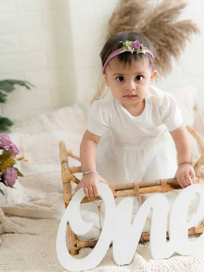 Standing tall and proud for her first birthday. This little girl looks so sweet in her white dress, surrounded by a beautiful bohemian-style setup.
