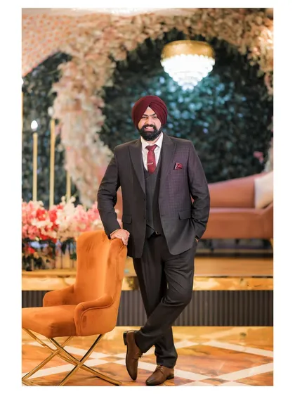 A confident, full-length portrait of the groom, Dipender, standing by a chair, showcasing his sharp attire.