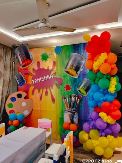A colorful and creative art party theme for Tanishka. The backdrop is a rainbow of colors, decorated with paint splatters, brushes, and a palette, all brought together with a vibrant balloon pillar.