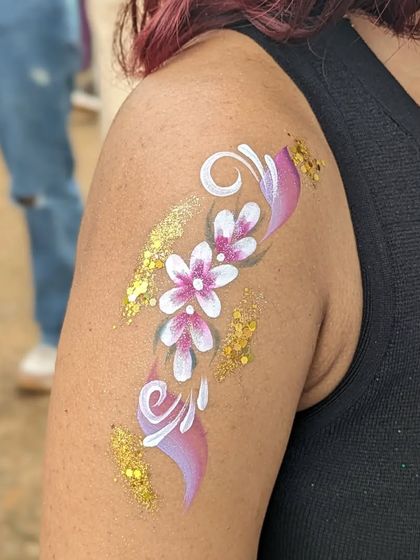A floral arm tattoo with pink flowers and a swirl of gold glitter.