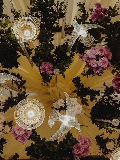 A view looking up at a ceiling installation, featuring hanging glass baubles, acrylic birds, and floral arrangements. This creates a sense of wonder and makes the space feel more intimate.
