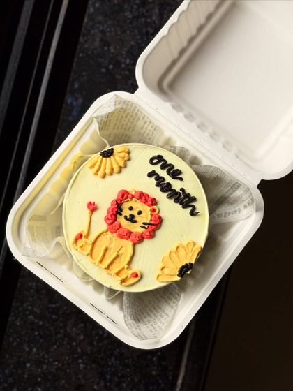 An adorable bento cake to celebrate a one-month milestone. This design features a cute, hand-piped lion cub on a soft yellow background, perfect for celebrating a new baby.