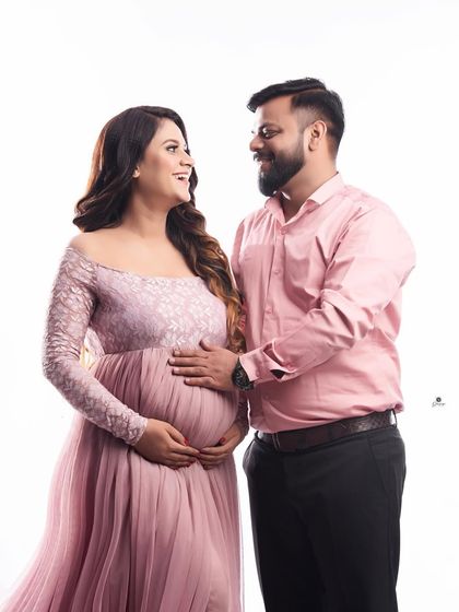 A classic couple portrait filled with warmth and affection. The coordinated pink outfits and the partner's gentle touch on the baby bump create a beautiful image of togetherness.