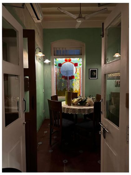 Looking into a private dining nook at The Lovefools, you see how color and light create a unique vibe. The green walls, stained-glass window, and lace tablecloth come together to form a cozy, romantic setting.
