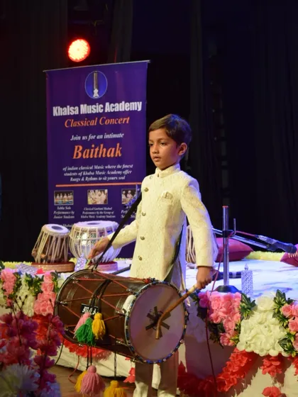 A full-length view of a young student performing on the dhol, a popular percussion instrument known for its high-energy beats.